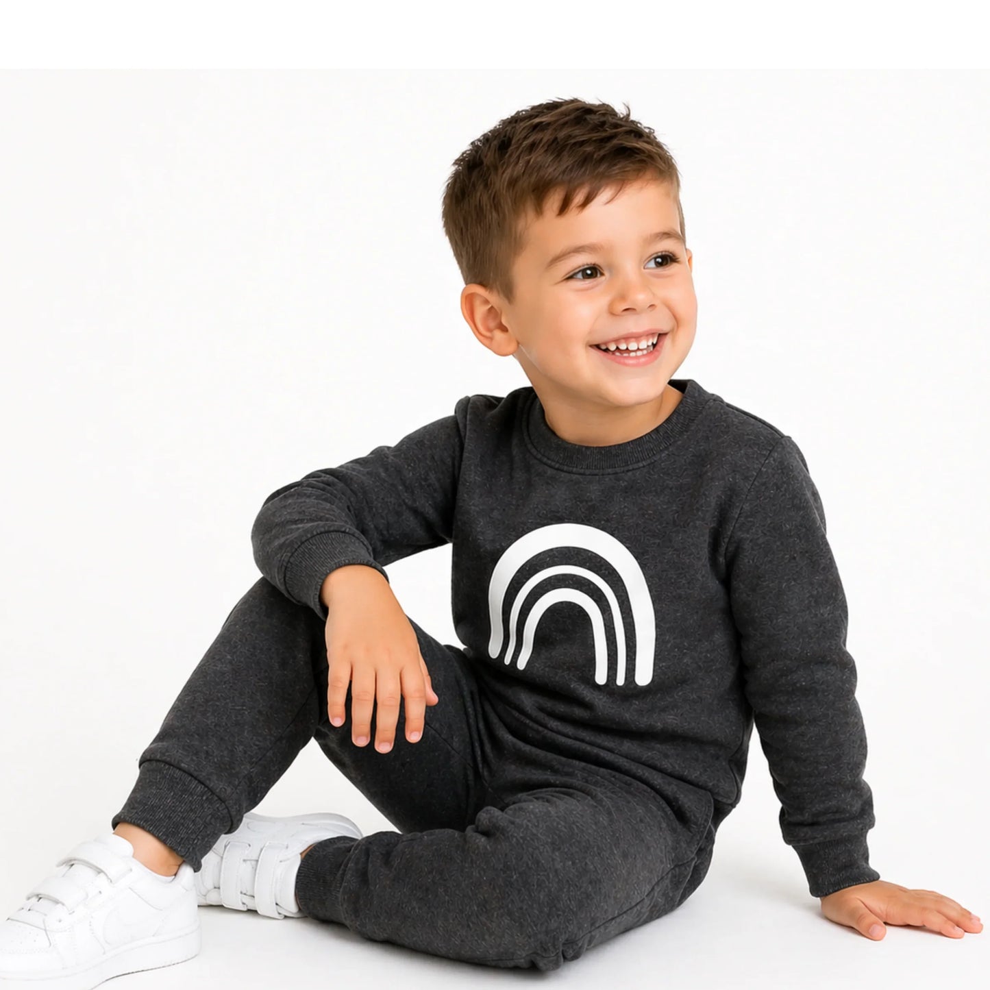 Smiling toddler in grey rainbow print sweatshirt and matching joggers, white sneakers, cozy kids tracksuit