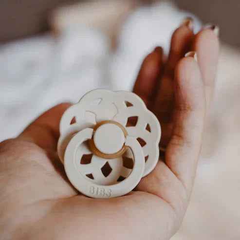Cream silicone pacifier with floral cutout design, held gently in hand for baby comfort