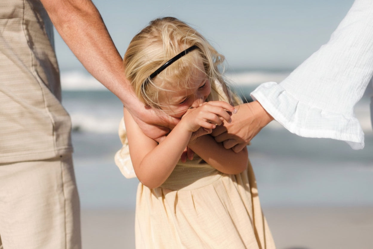 Child in a yellow dress being comforted by an adult on a beach