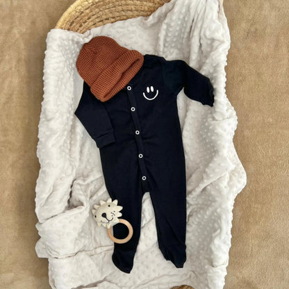 Black baby onesie with smiley face, brown knit hat, and lion teether on white minky blanket